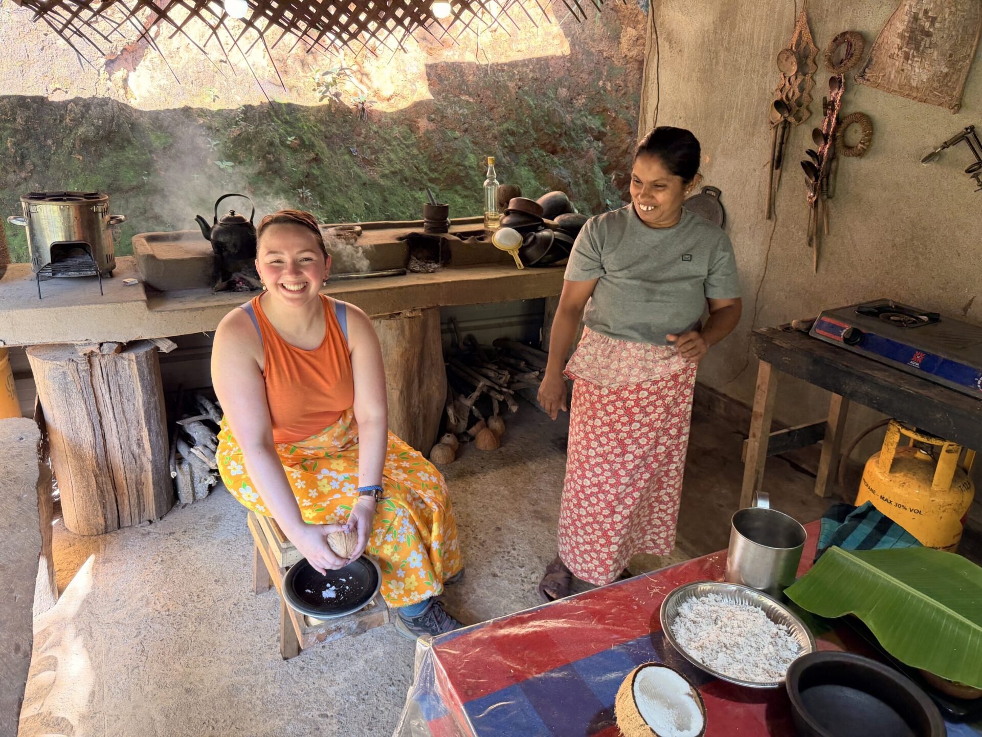 A traveller preparing fresh coconut with a local woman in a traditional Sri Lankan kitchen.