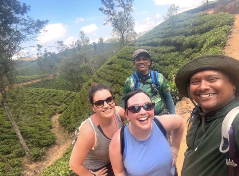 Four smiling walkers taking a group photograph among the tea plantations of Sri Lanka's hill country.