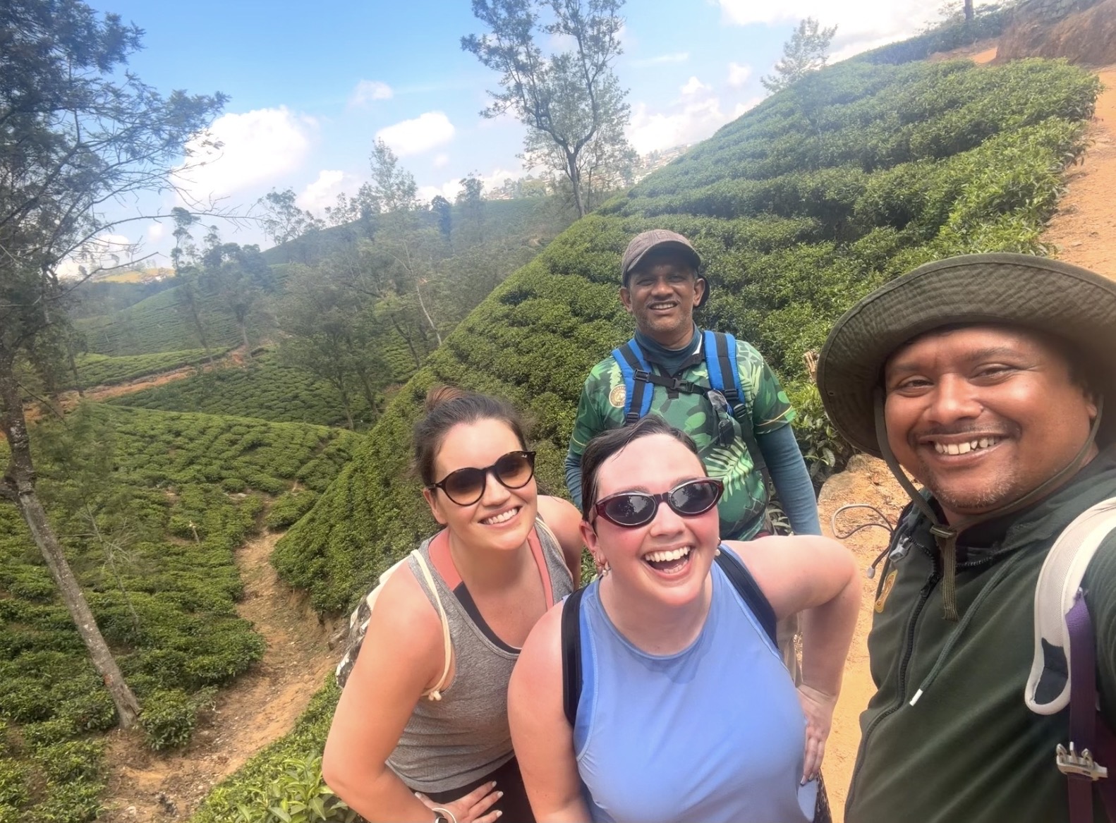 Four smiling walkers taking a group photograph among the tea plantations of Sri Lanka's hill country.