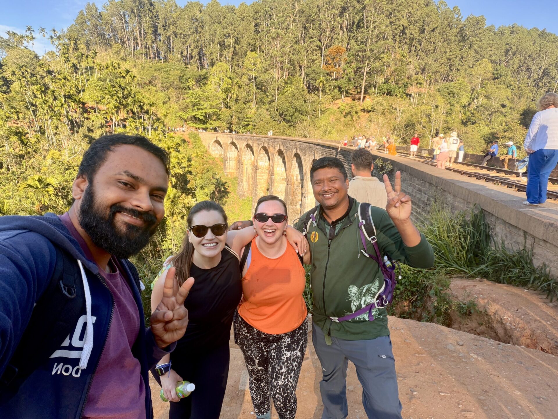 Four travellers posing beside the Nine Arch Bridge in Ella, surrounded by lush green forest.
