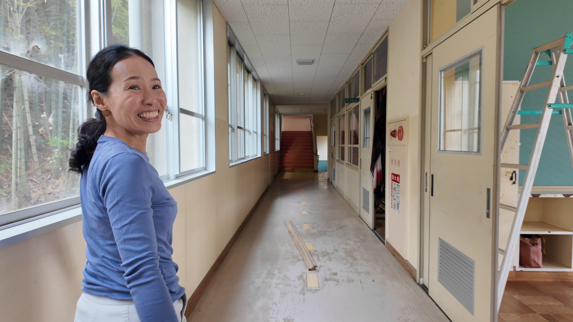 Mihoko Christie smiling in the corridor of a converted school building used for community activities in rural Japan.