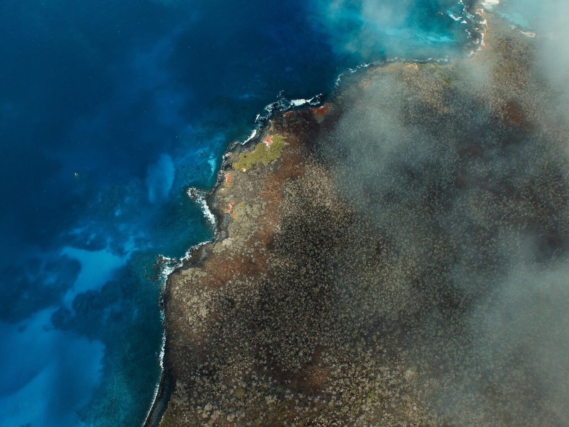 Aerial view of the rugged volcanic coastline of Floreana Island surrounded by deep blue Pacific waters.