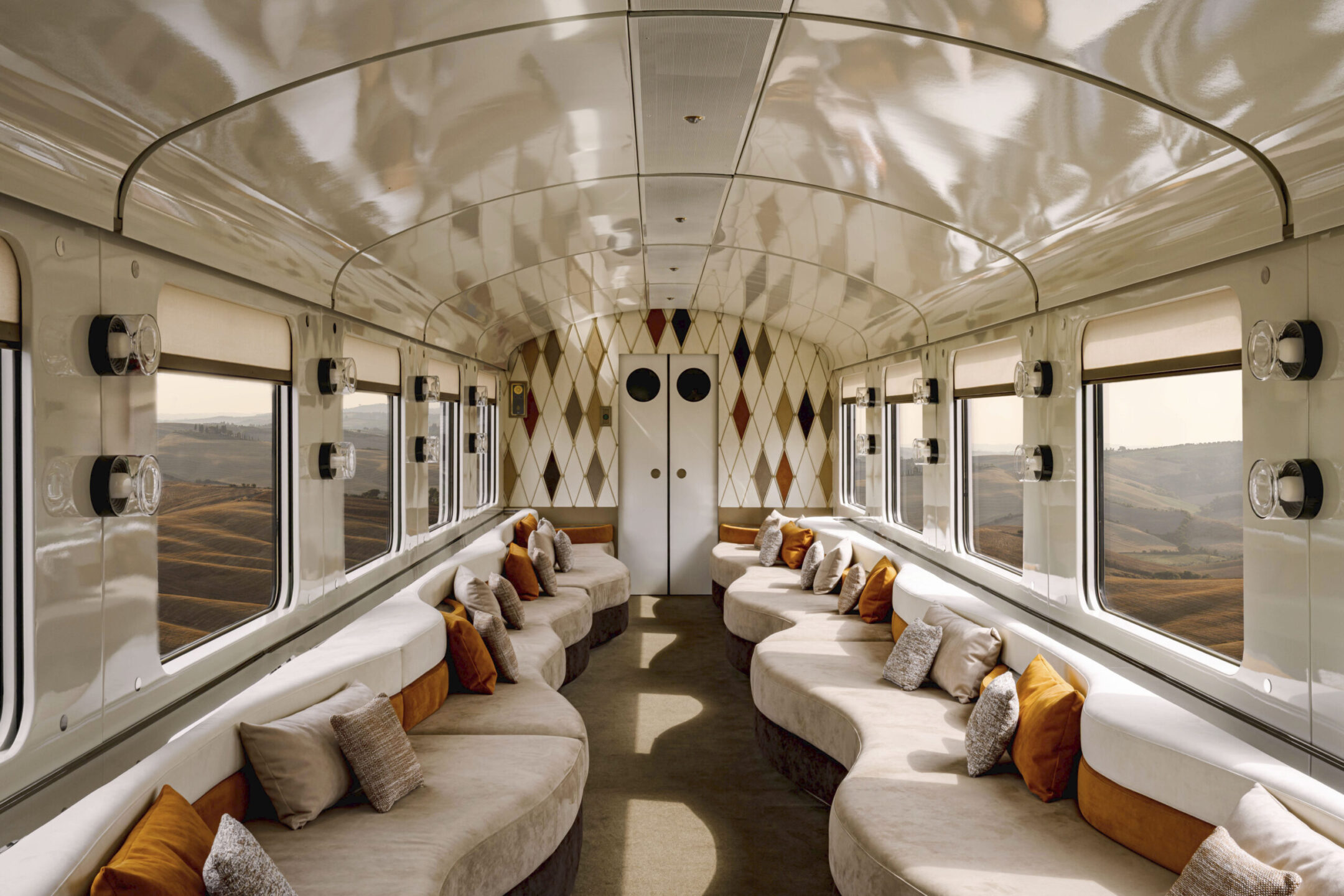 Elegant lounge carriage aboard La Dolce Vita Orient Express, with curved sofas and views of the Italian countryside.