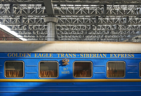 Blue and gold Golden Eagle luxury train carriage standing beneath the roof of a railway station.